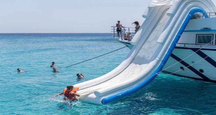 Holidaymakers slide from a yacht into clear turquoise sea while others swim nearby