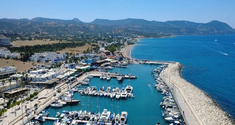 Drone view of modern marina filled with yachts beside a long sandy coastline and mountains
