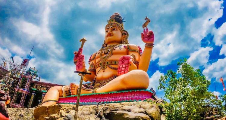 Lebendige Riesenstatue einer hinduistischen Gottheit, die symbolische Gegenstände vor einem strahlend blauen Himmel hält.