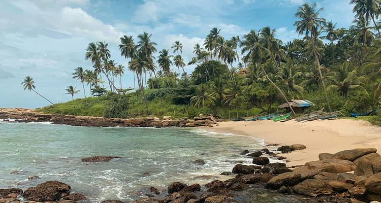 Tropical cove with palm-lined sandy beach, turquoise water and small fishing boats on shore