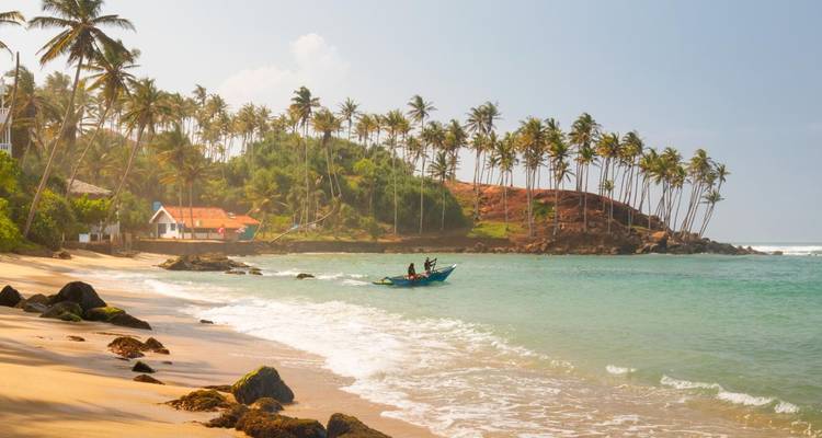 Sunny tropical beach with gentle waves, palm trees and fishermen in a small boat offshore