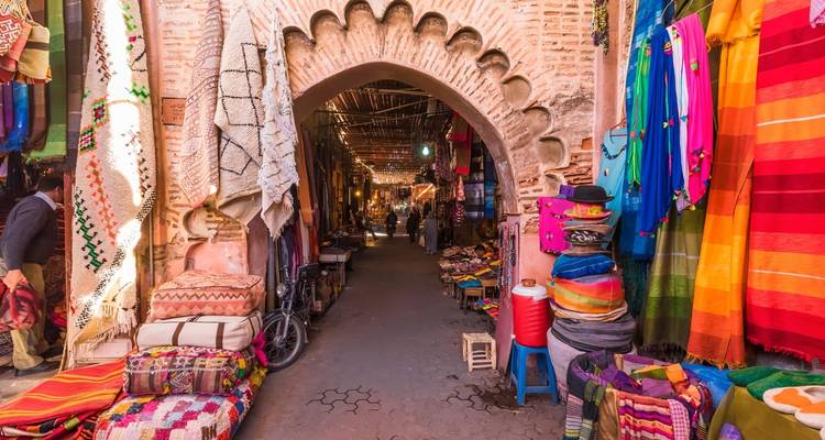 Callejón colorido del zoco en Marrakech con textiles y alfombras colgando junto a una puerta arqueada