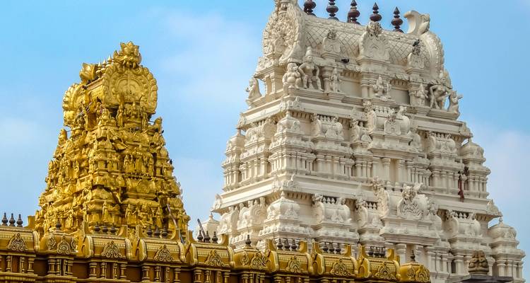 Close-up of ornate gopurams, one gilded and one white, adorned with intricate sculptures against a clear sky.