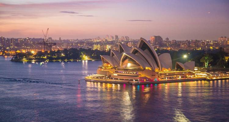 Iconische Sydney Opera House verlicht bij schemering naast glinsterend havenwater
