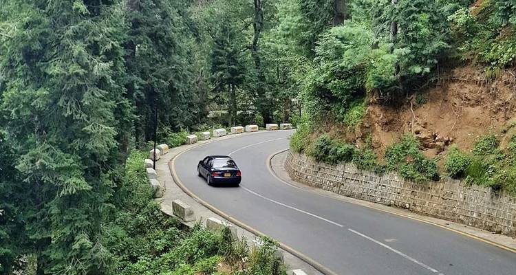 Winding mountain road through evergreen forest with solitary car driving uphill