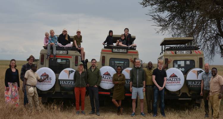 Große Safari-Gruppe steht vor drei Jeeps auf offener Graslandschaft für ein Gruppenfoto