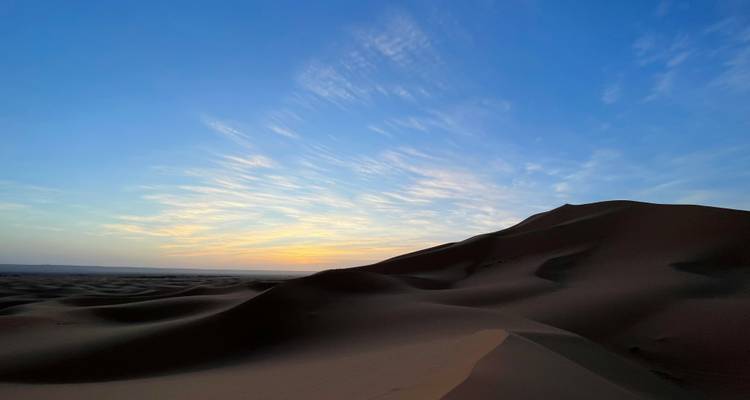 Paisaje desértico sereno al amanecer con dunas ondulantes silueteadas contra un cielo colorido de amanecer
