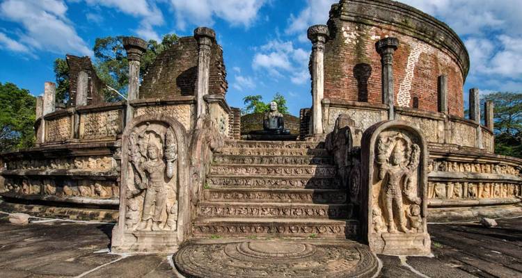 Alte Steinstufen und geschnitzte Reliefs, die zu einem kreisförmigen Backsteinschrein mit einer sitzenden Buddha-Statue führen.