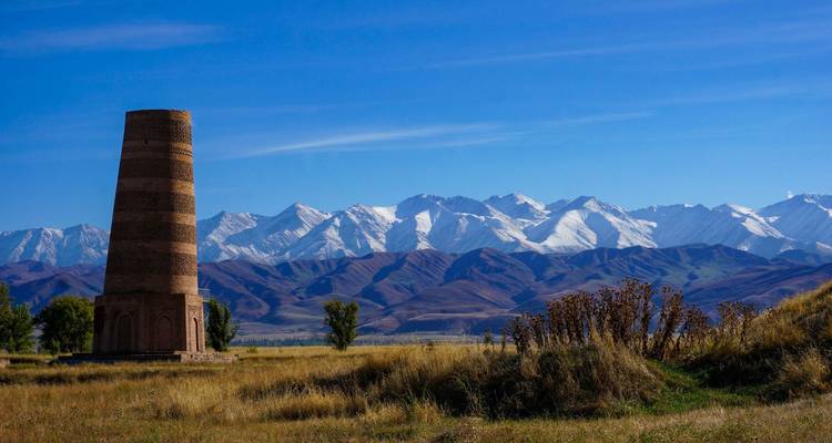 La tour de Burana, ancienne structure de brique, s'élève sur des prairies ouvertes avec les pics enneigés du Tian Shan s'étendant à l'horizon.