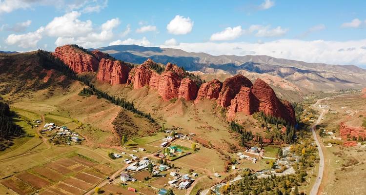 Les impressionnantes falaises de grès rouge de Jeti-Oguz s'élèvent au-dessus d'une vallée rurale parsemée de petites maisons et de champs.