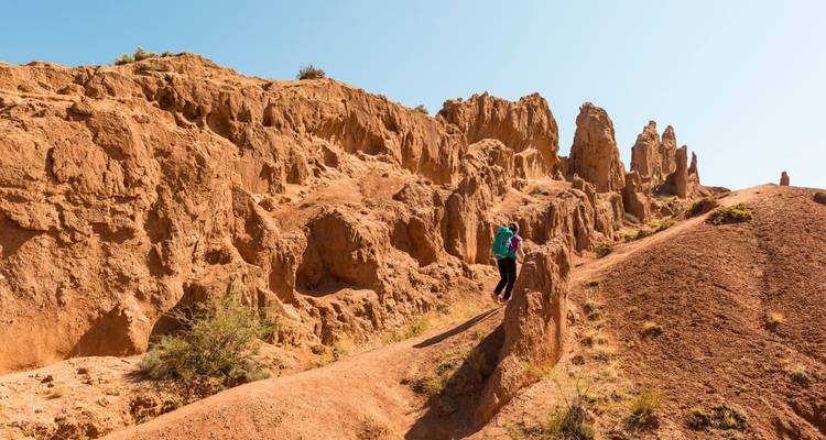 Un randonneur solitaire explore les pics et les crêtes de roche rousse du Canyon des Contes de Fées sous un ciel bleu dégagé.