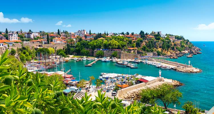 Ville portuaire pittoresque avec des bateaux et des maisons aux toits de tuiles entourant une baie turquoise.