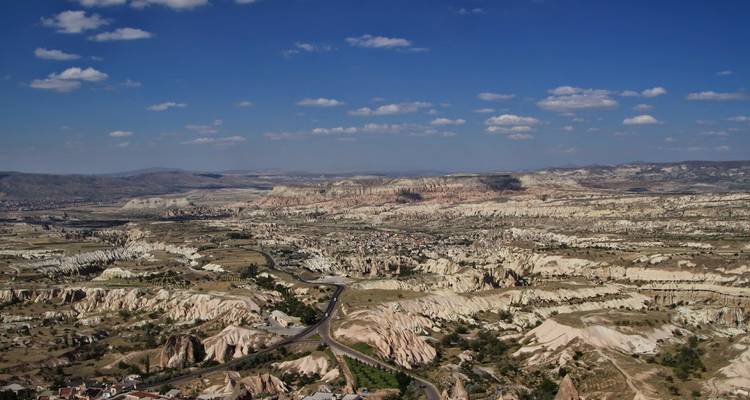 Vaste panorama aérien des vallées couleur miel de la Cappadoce et des formations rocheuses en cheminées de fées sous un ciel bleu.