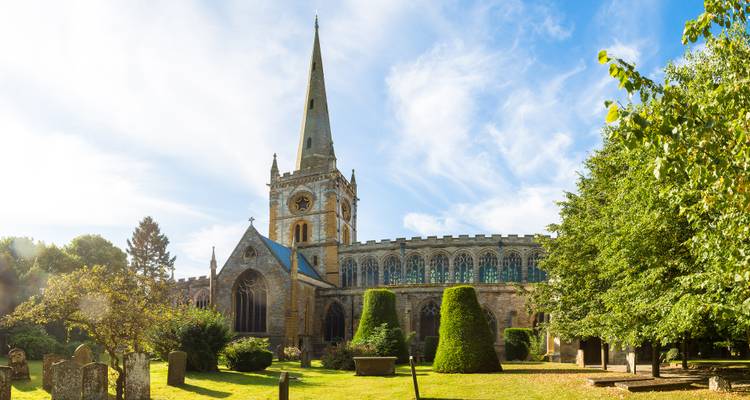 Historic stone church with tall spire and manicured garden bathed in warm morning light.