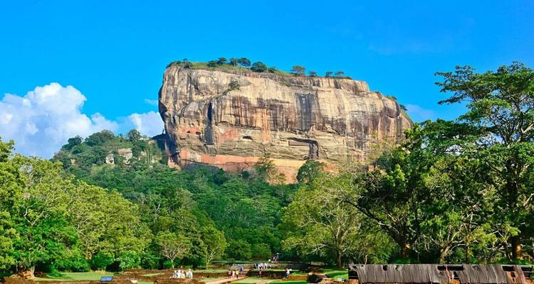 Der ikonische Sigiriya-Felsen erhebt sich dramatisch über smaragdgrünen Wald unter einem strahlend blauen Himmel.