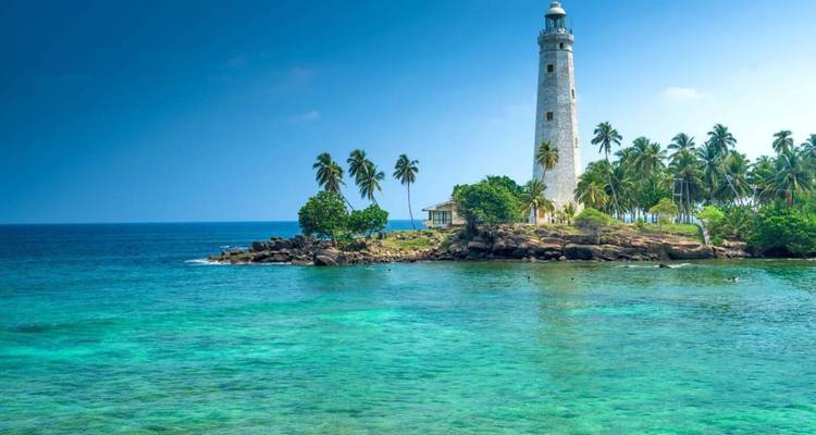 Weißer Leuchtturm steht auf einer winzigen palmengesäumten Insel, umgeben von kristallklarem türkisfarbenem Meer.