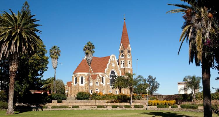 Stenen Christuskirche kerk met rood dak omlijst door hoge palmbomen onder heldere blauwe lucht