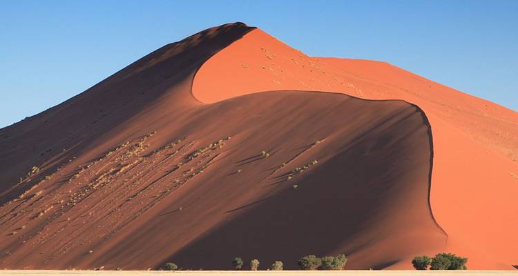 Dichtbij beeld van een steile oranje zandduinen met scherpe richel tegen blauwe lucht