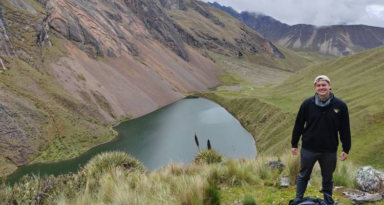 Randonneur solitaire souriant au bord d'un lac alpin entouré de pentes escarpées multicolores.
