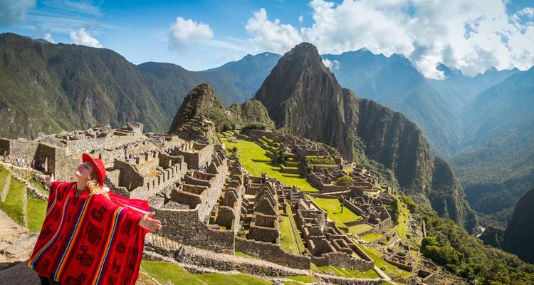 Voyageur en poncho rouge vif étendant joyeusement les bras en contemplant les terrasses emblématiques du Machu Picchu et le pic imposant d'Huayna Picchu.