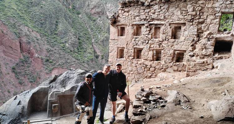 Petit groupe souriant devant les ruines de greniers incas à flanc de falaise surplombant une gorge verdoyante.