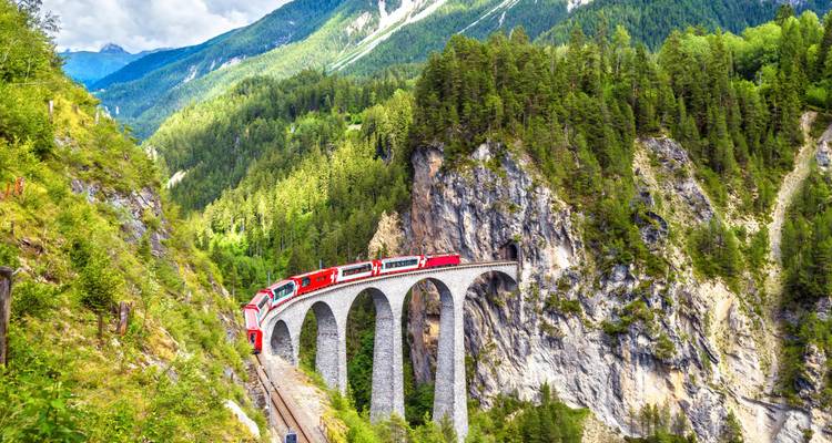 Train alpin iconique de couleur rouge traversant les spectaculaires arches de pierre du viaduc de la Landwasser au milieu des majestueuses montagnes suisses.