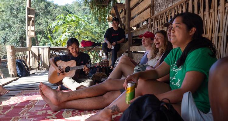 Travellers relaxing on wooden platform while local plays guitar in jungle setting