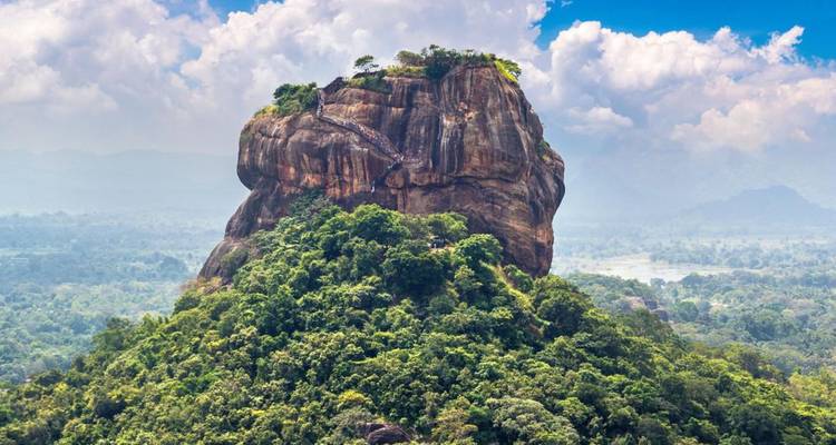 Drohnenaufnahme des üppigen, waldbedeckten Sigiriya-Felsens, der sich unter dramatischen Wolken über die umliegenden Ebenen erhebt.