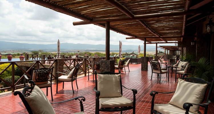 Überdachte Terrasse mit gepolsterten Stühlen mit Blick auf sanfte Hügel und Lodgegelände.