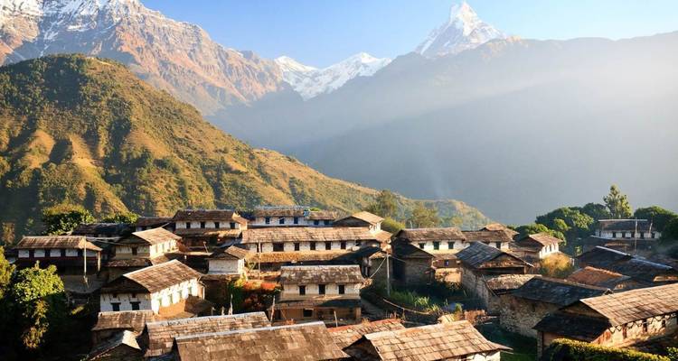 Traditionele stenen huizen van een Himalaya-dorp baden in gouden ochtendlicht onder besneeuwde toppen.