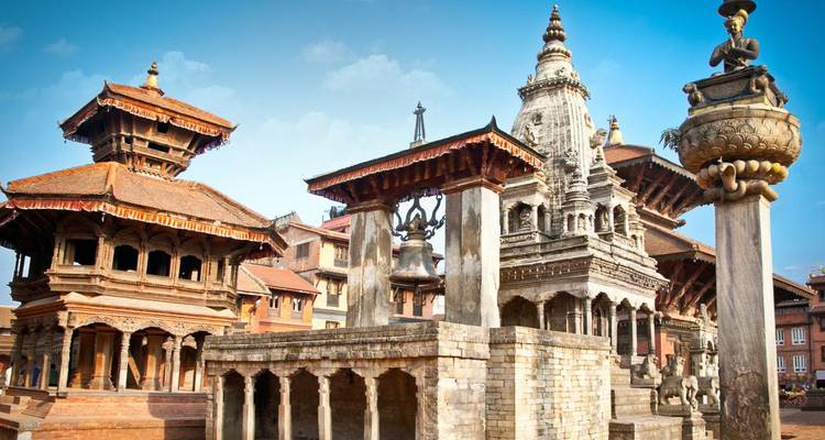 Historische tempels en stenen zuilen van Bhaktapur Durbar Square onder een heldere blauwe hemel.