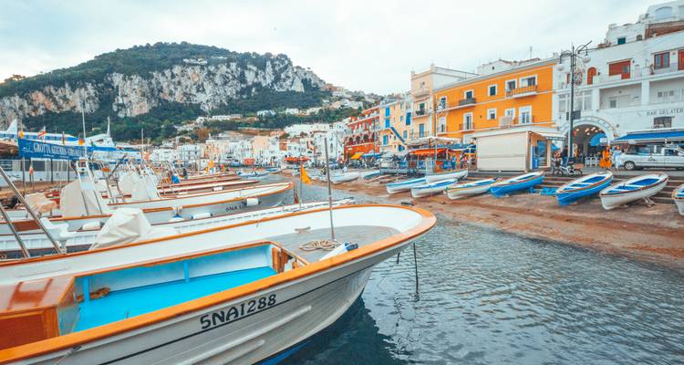 Bunte Fischerboote reihen sich im lebhaften Marina Grande von Capri mit dem Hügeldorf im Hintergrund auf.