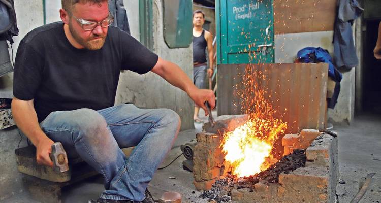 Blacksmith hammering red-hot metal on an anvil as sparks fly inside a small workshop