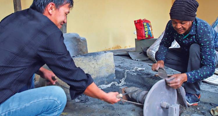Artisans grinding a blade on a stone wheel inside a traditional forge