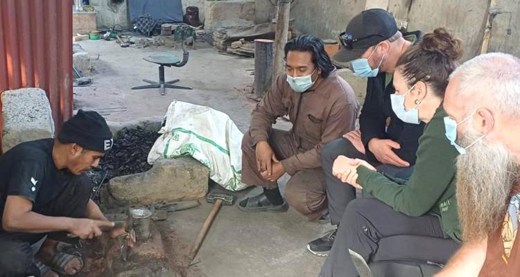 Small tour group wearing masks observing a blacksmith demonstration inside a workshop
