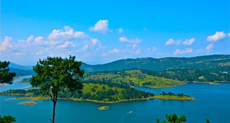 Expansive blue lake dotted with green islands under a clear sky in Meghalaya hills.