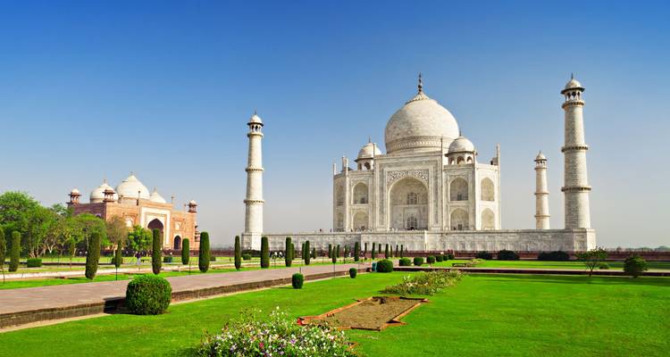 Le marbre blanc immaculé du Taj Mahal brille sous un ciel bleu dégagé, reflété par des jardins soignés et des canaux d'eau.