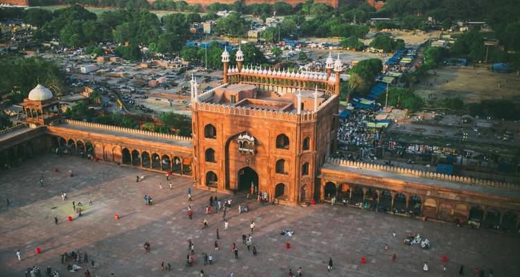 Une perspective aérienne de la Jama Masjid montre sa porte monumentale ouvrant sur une vaste cour remplie de visiteurs.