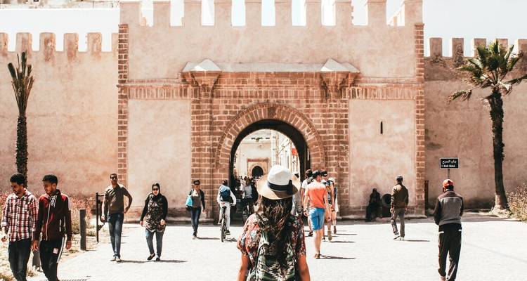 Tourists walking toward an arched city gate set in historic walls of Essaouira medina.