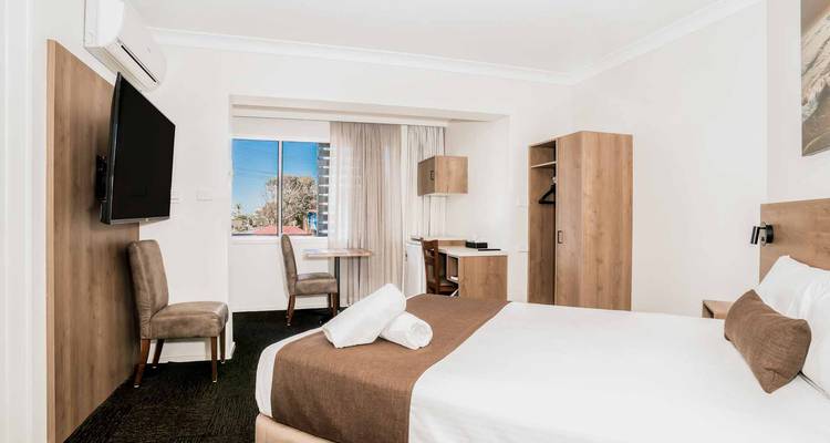 Chambre d'hôtel moderne et minimaliste avec lit double, bureau et grande télévision donnant sur la vue de la ville.