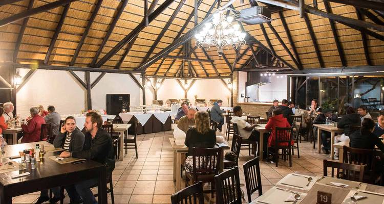 Scène de dîner animée à l'intérieur d'un restaurant de lodge au toit de chaume avec des voyageurs qui dînent et bavardent.