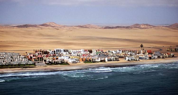 Une rangée de maisons côtières colorées s'étend entre les dunes de désert vallonnées et les vagues de l'Atlantique.