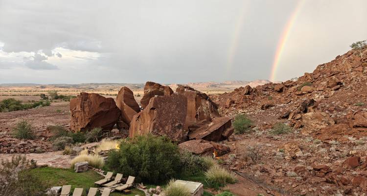 Des rochers rouges escarpés et un lodge du désert se dressent sous un double arc-en-ciel après le passage d'un orage.