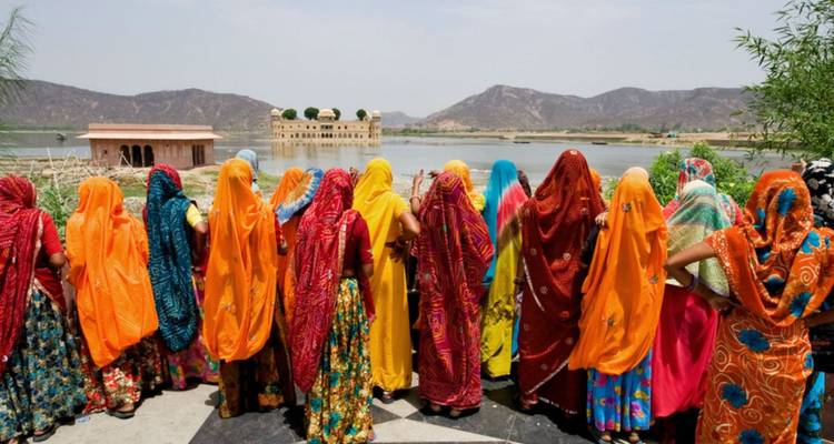 Vrouwen in levendige sari's bewonderen het Jal Mahal meerpaleis vanaf een uitkijkpunt aan de oever.