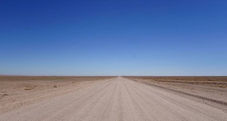 Een rechte grindweg verdwijnt naar de horizon onder een diepblauwe hemel.