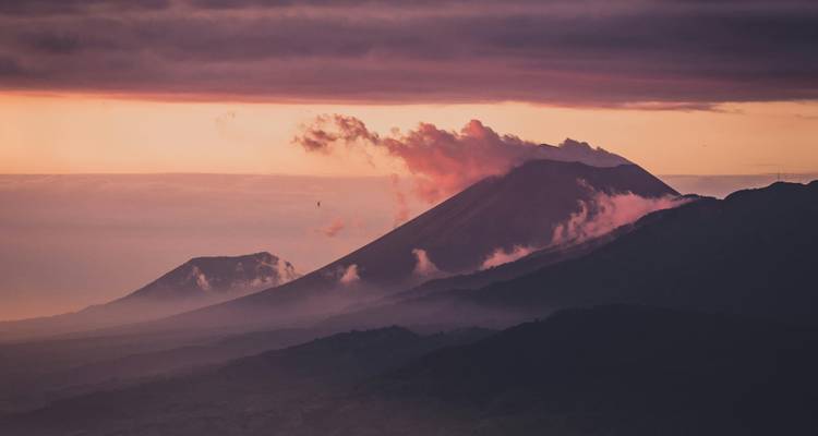 Volcanic cones emitting pink steam at sunrise with layered ridges in Nicaragua.