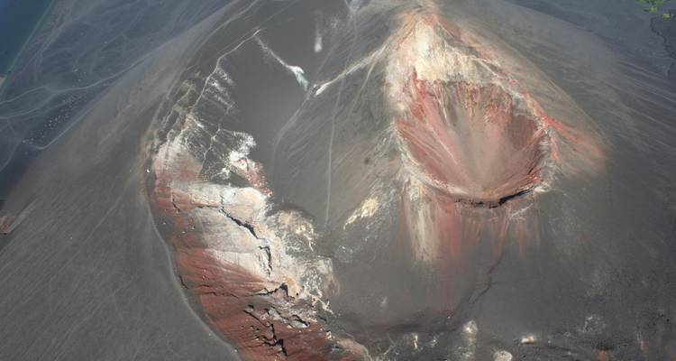 Overhead shot of eroded volcanic crater with colorful ash layers and fissures.
