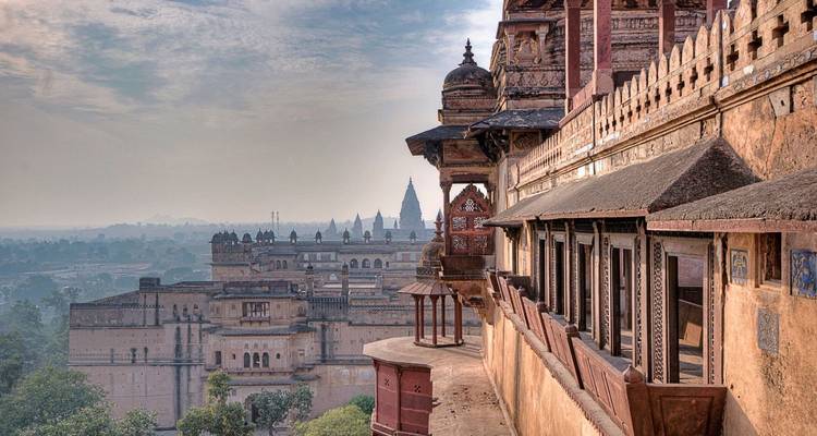 Ornate historic palace balconies overlook a hazy townscape of domes and temples at sunrise.