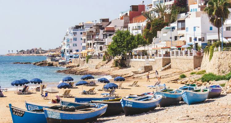 Golden sand beach dotted with blue fishing boats, umbrellas and white seaside village.