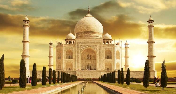 Taj Mahal en zijn spiegelvijver gebaad in gouden zonsondergangslicht met dramatische wolken erboven.